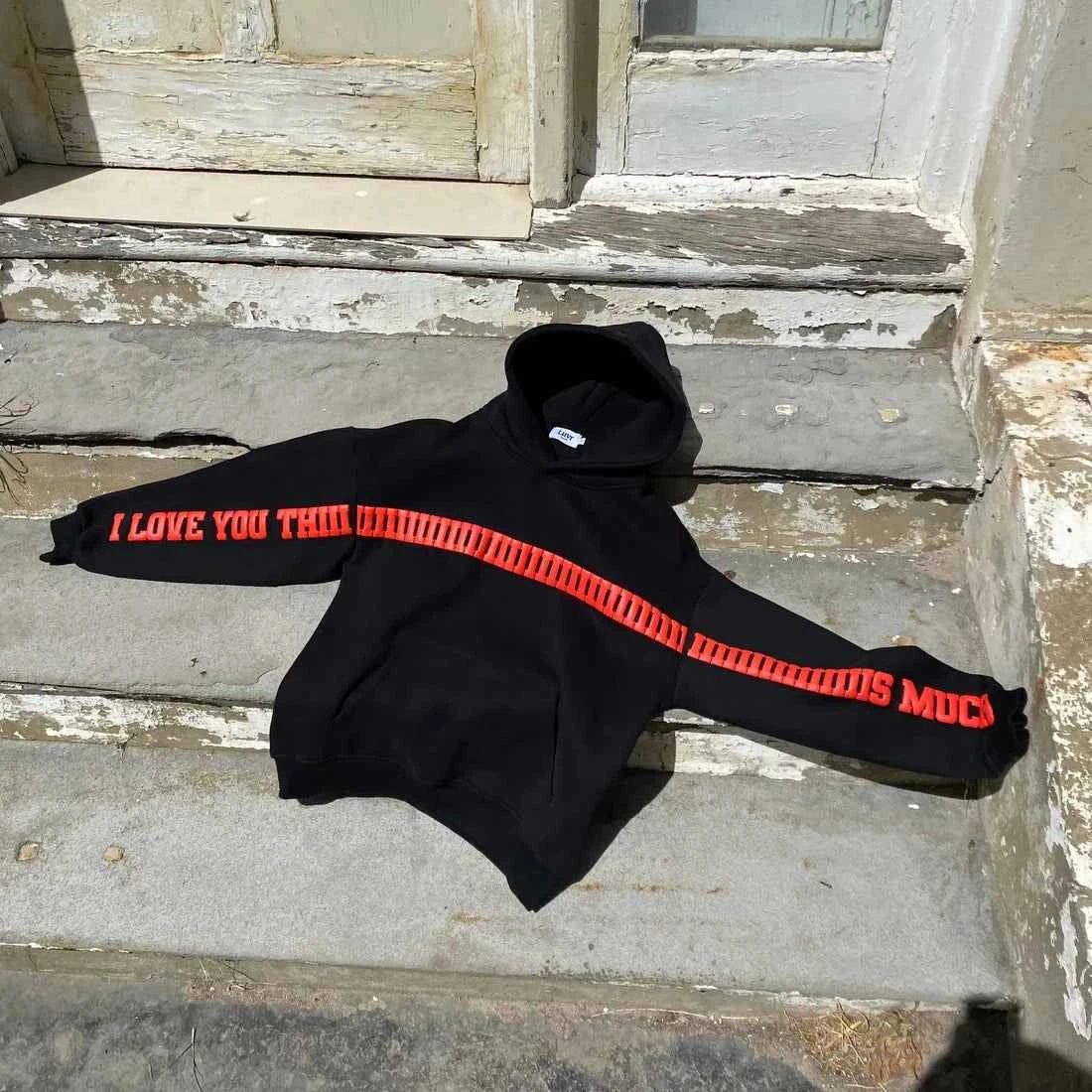 Elevate Your Style with the I Love You This Much Hoodie in Black by Xoratic, a black Hoodie with bold red lettering displayed on concrete steps