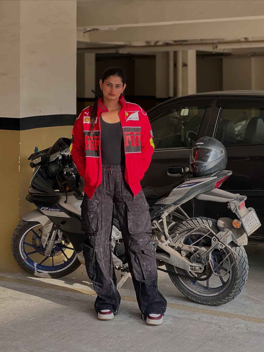 Ferrari Racing Jacket Red - Unleash Your Motorsport Spirit with Style by Xoratic, woman wearing a red racing jacket beside motorcycles in a parking area